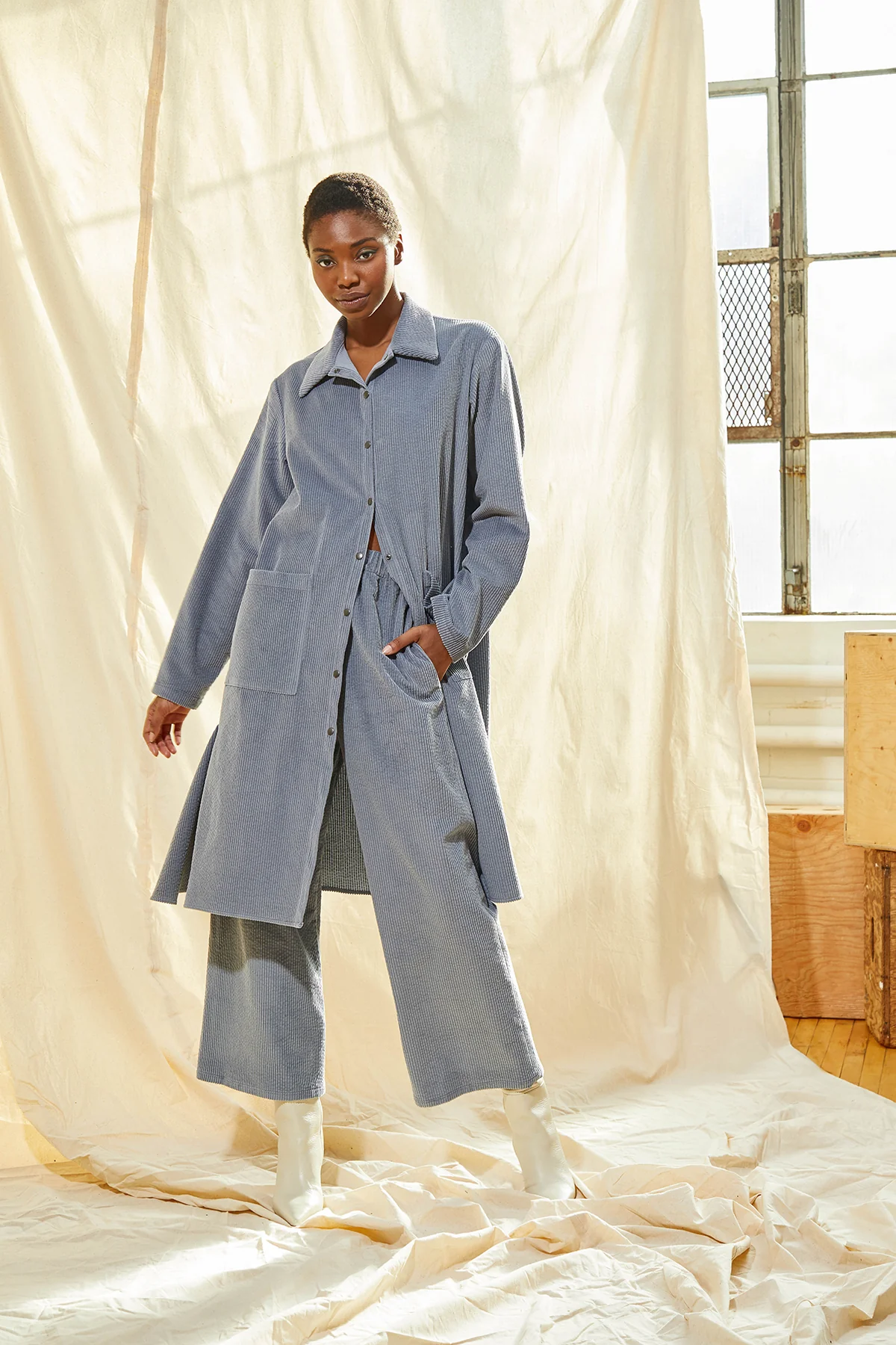 Woman wearing grey corduroy pant suit with beige background.